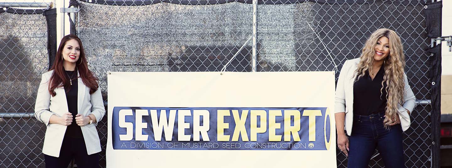 Two women business owners standing on either side of their company sign Sewer Experts