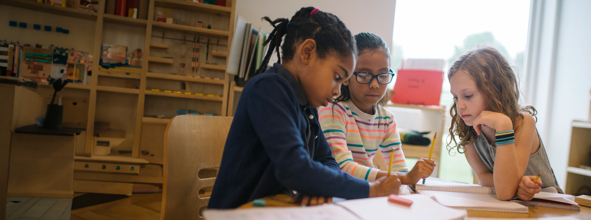 Three girls sitting at a table in an elementary classroom working on a project.