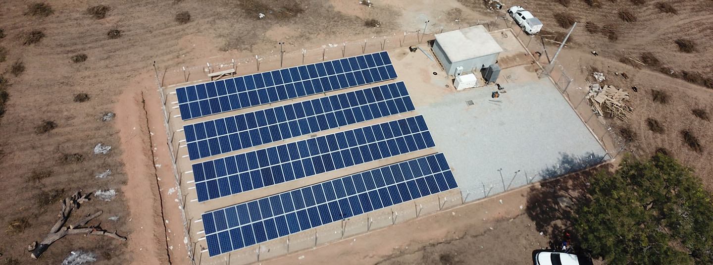 Group of four rows of solar panels surrounded by a fence next to a small building in Nigeria