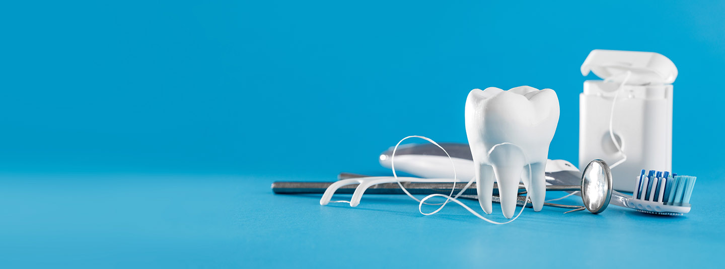 Dental mirror, toothbrush, floss and model of a molar with a blue background