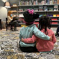 Two elementary students sitting on a floor with their arms around each other