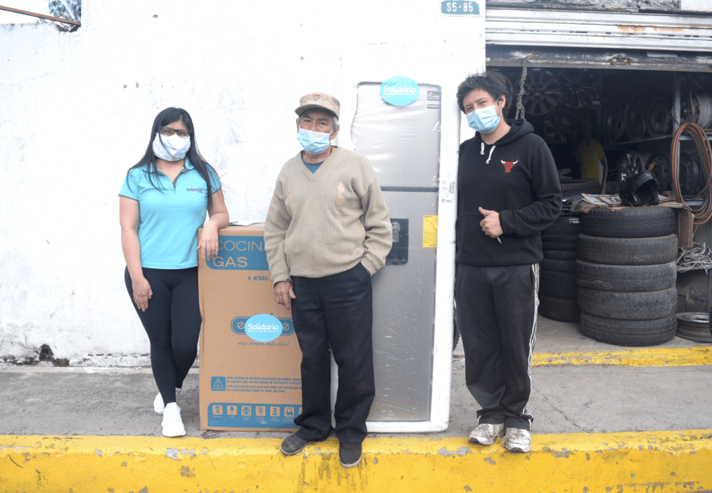 Three people standing in front of a buidling with a garage door open with a stack of ties