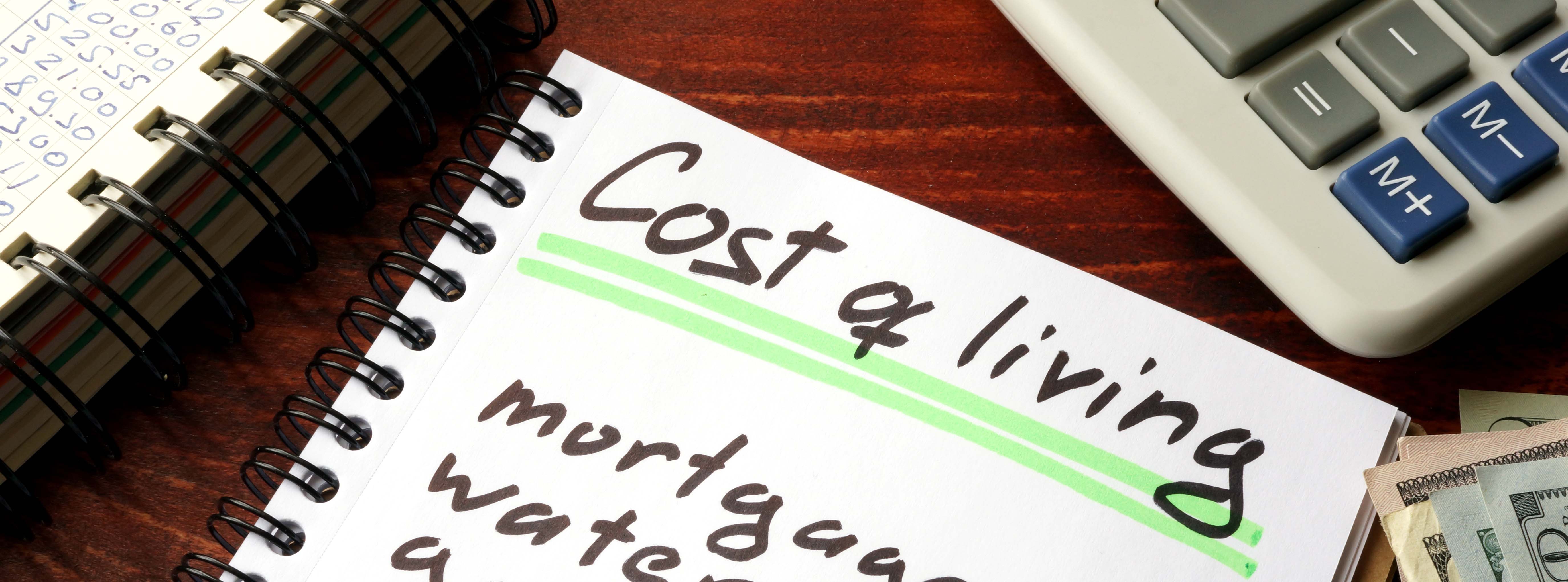 Cost of living written on a spiral notepad surrounded by a calculator and money